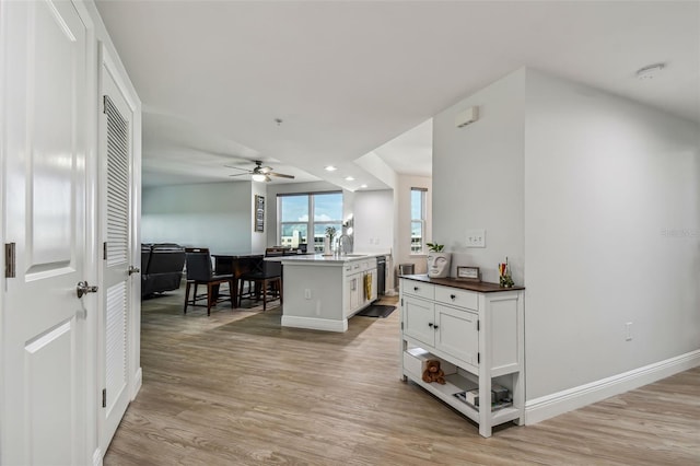 kitchen featuring dishwasher, a kitchen island with sink, white cabinets, ceiling fan, and light wood-type flooring