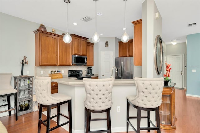 kitchen featuring light hardwood / wood-style flooring, stainless steel appliances, decorative light fixtures, and a breakfast bar area