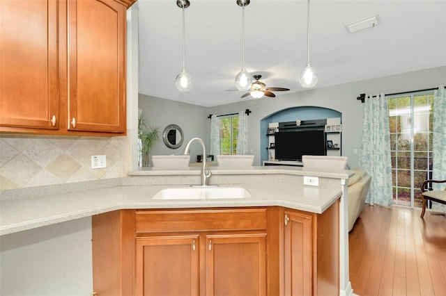 kitchen with light wood-type flooring, sink, kitchen peninsula, ceiling fan, and decorative backsplash