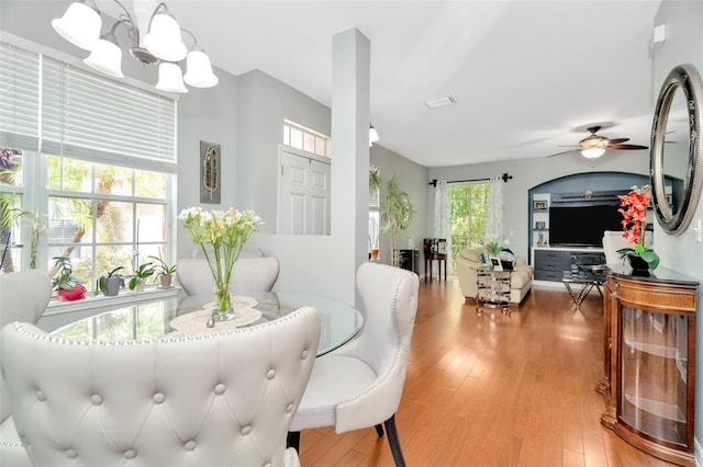 dining space with ceiling fan with notable chandelier, a wealth of natural light, and light hardwood / wood-style floors