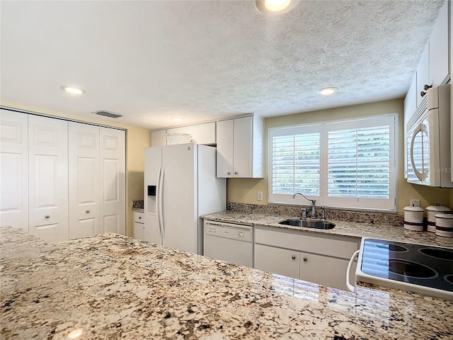 kitchen with white cabinetry, white appliances, a textured ceiling, light stone counters, and sink