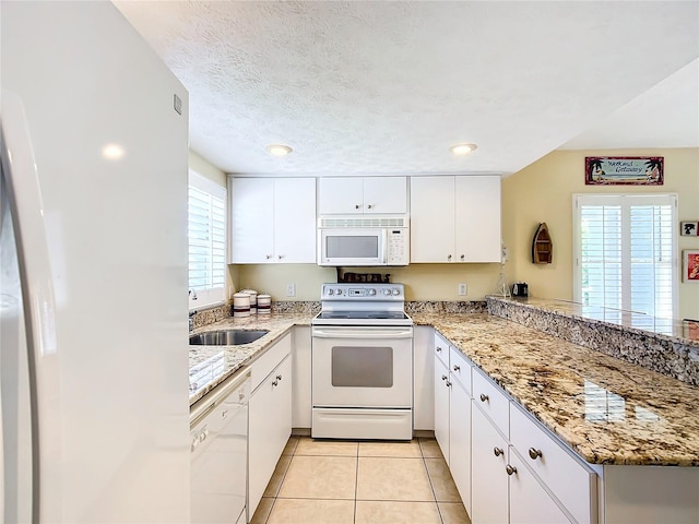 kitchen featuring white appliances, light tile patterned floors, kitchen peninsula, sink, and white cabinets