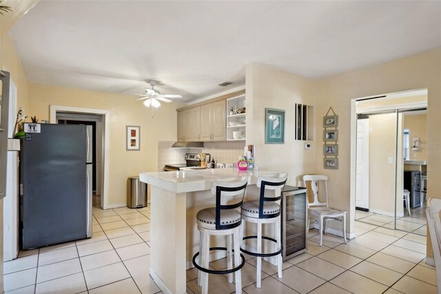 kitchen with decorative backsplash, light tile patterned floors, appliances with stainless steel finishes, a kitchen bar, and kitchen peninsula