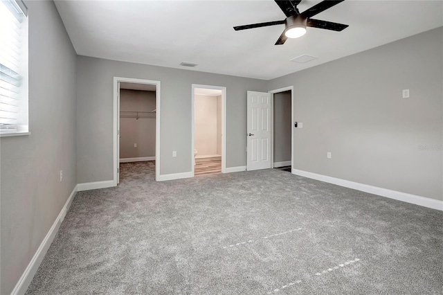 unfurnished bedroom featuring multiple windows, a walk in closet, ceiling fan, and a closet