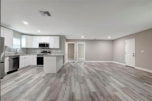 kitchen with light stone countertops, appliances with stainless steel finishes, white cabinetry, and light hardwood / wood-style floors