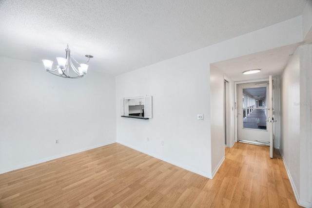 empty room with a textured ceiling, an inviting chandelier, and light hardwood / wood-style floors