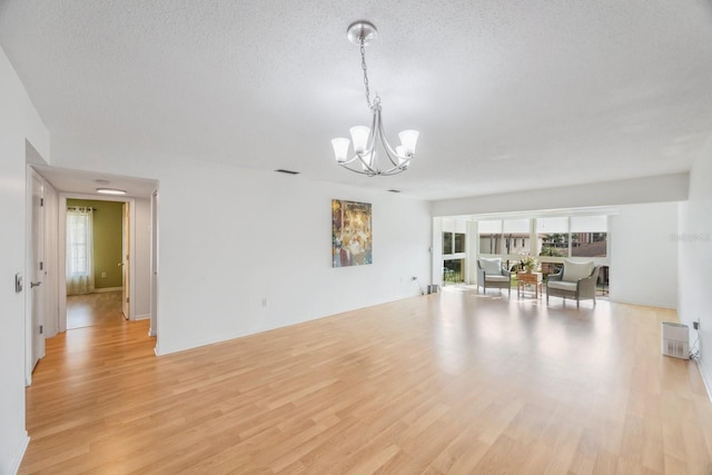 unfurnished living room featuring light wood-type flooring, a textured ceiling, and a chandelier