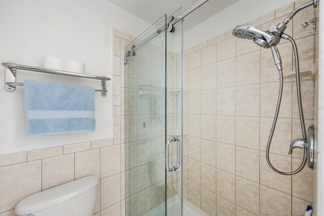 bathroom featuring a shower with shower door, toilet, and tile walls