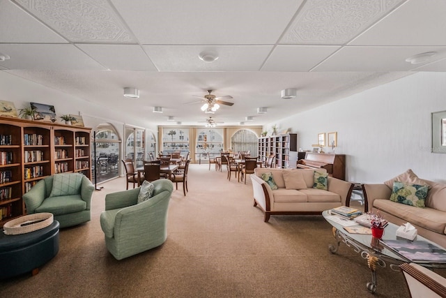 living room with ceiling fan, carpet floors, and a drop ceiling