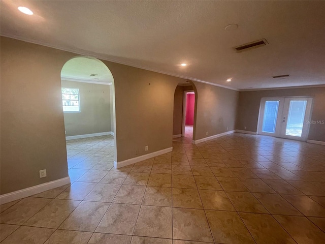 empty room with a textured ceiling, light tile patterned flooring, and ornamental molding