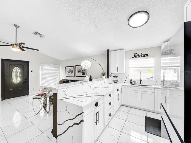 kitchen featuring kitchen peninsula, white cabinetry, lofted ceiling, ceiling fan, and light stone counters