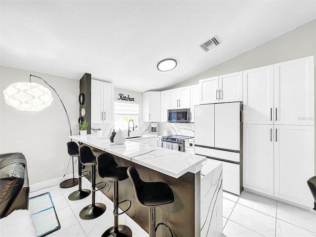 kitchen featuring tasteful backsplash, light stone countertops, appliances with stainless steel finishes, lofted ceiling, and white cabinets