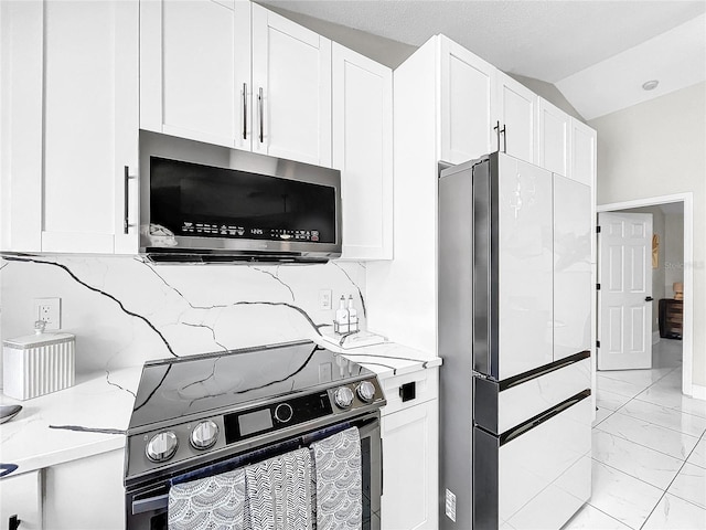 kitchen featuring vaulted ceiling, light stone countertops, backsplash, appliances with stainless steel finishes, and white cabinets