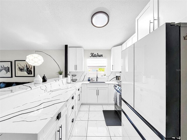 kitchen featuring white fridge, light stone counters, white cabinetry, and sink