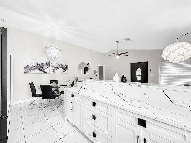 kitchen with ceiling fan with notable chandelier, light stone countertops, hanging light fixtures, lofted ceiling, and white cabinets