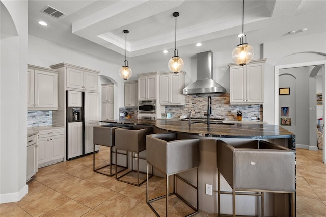 kitchen with a raised ceiling, wall chimney exhaust hood, a breakfast bar area, and appliances with stainless steel finishes