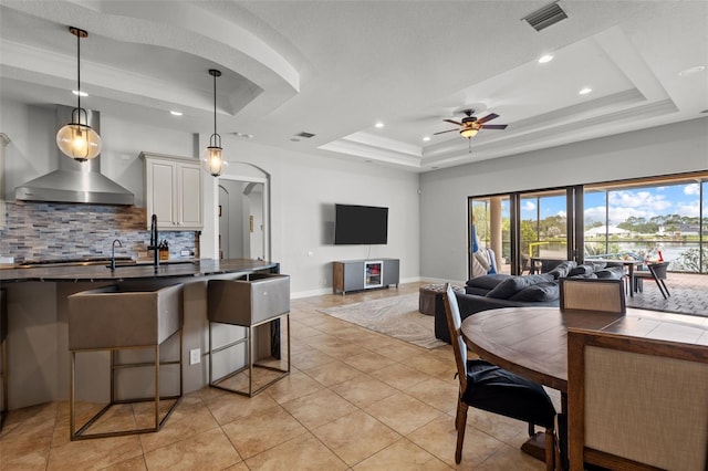 kitchen with ceiling fan, decorative light fixtures, a tray ceiling, light tile patterned floors, and a kitchen bar