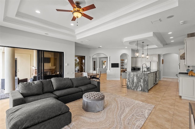 tiled living room featuring a raised ceiling, ceiling fan, sink, and ornamental molding