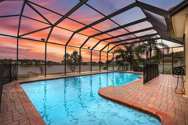 pool at dusk featuring a water view, a patio, and glass enclosure