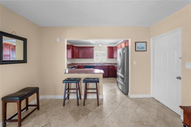 kitchen with a breakfast bar, sink, dishwashing machine, kitchen peninsula, and stainless steel refrigerator