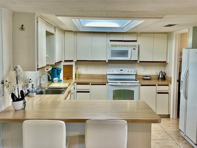 kitchen featuring white appliances, sink, kitchen peninsula, light tile patterned flooring, and a kitchen breakfast bar