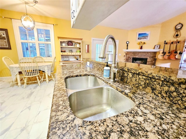 kitchen with white cabinetry, decorative light fixtures, a brick fireplace, sink, and stone countertops