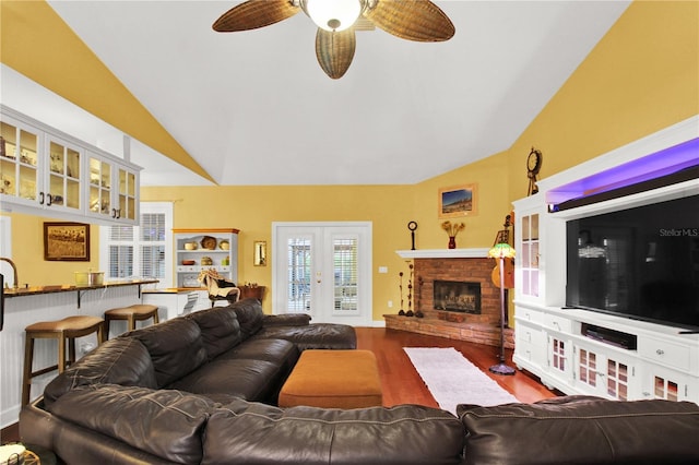 living room featuring lofted ceiling, ceiling fan, hardwood / wood-style flooring, and a brick fireplace