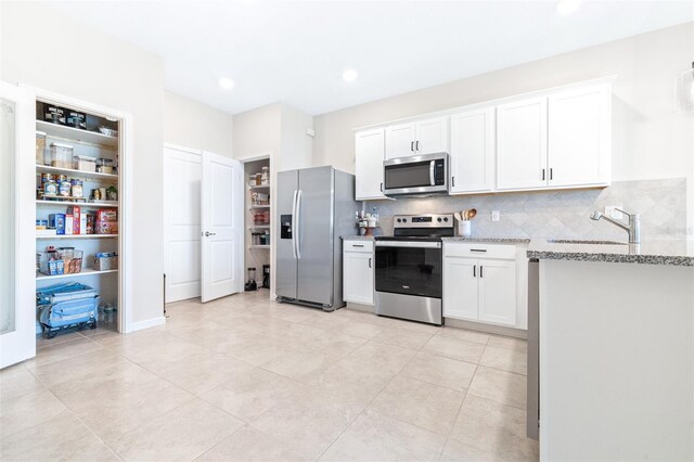 kitchen featuring light tile patterned floors, stainless steel appliances, sink, white cabinetry, and light stone counters