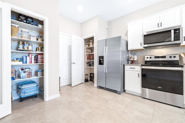 kitchen with white cabinets, appliances with stainless steel finishes, light tile patterned floors, and decorative backsplash