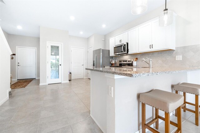 kitchen with white cabinets, hanging light fixtures, backsplash, light stone counters, and stainless steel appliances