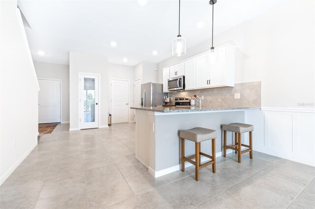 kitchen with light stone counters, stainless steel appliances, white cabinetry, kitchen peninsula, and decorative backsplash