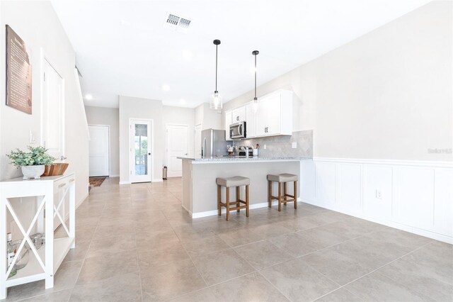 kitchen featuring stainless steel appliances, a kitchen breakfast bar, kitchen peninsula, decorative backsplash, and white cabinets