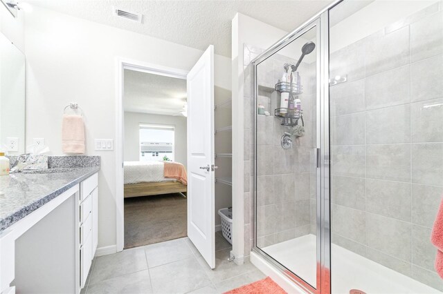 bathroom with a shower with door, vanity, tile patterned flooring, and a textured ceiling