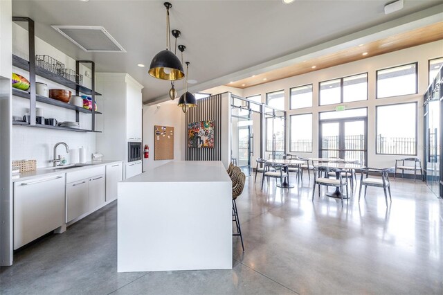 kitchen with white cabinets, a center island, dishwashing machine, decorative light fixtures, and concrete flooring