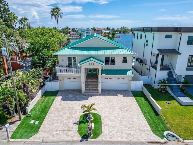 coastal home featuring a garage, stairs, decorative driveway, a front lawn, and a standing seam roof