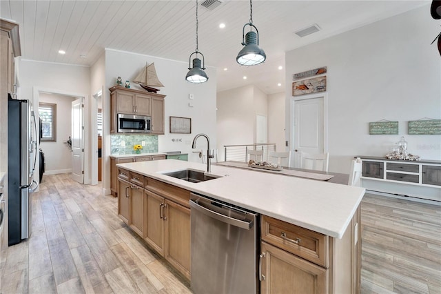 kitchen featuring decorative light fixtures, appliances with stainless steel finishes, light hardwood / wood-style floors, sink, and a center island with sink