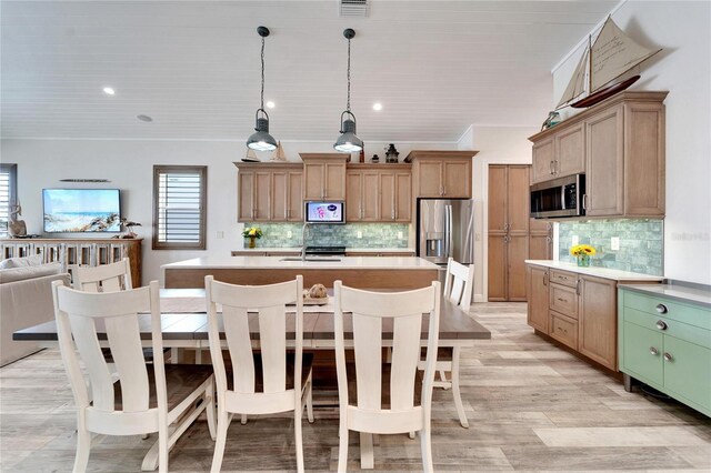 kitchen featuring a kitchen island with sink, backsplash, stainless steel appliances, and decorative light fixtures