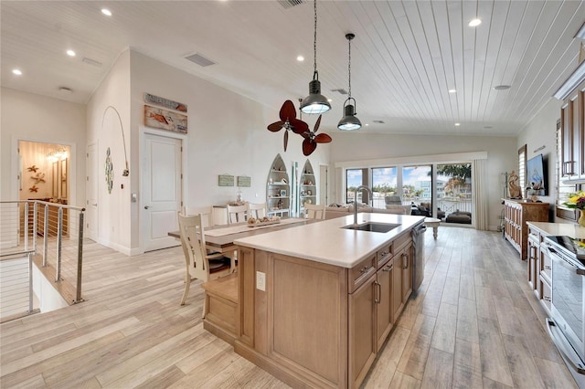 kitchen featuring vaulted ceiling, light hardwood / wood-style floors, an island with sink, hanging light fixtures, and sink