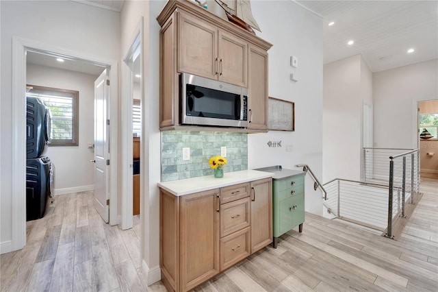 kitchen featuring light wood-style floors, stacked washer / drying machine, light countertops, backsplash, and stainless steel microwave