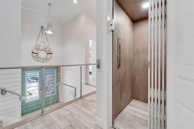 hall with lofted ceiling, light hardwood / wood-style floors, and elevator