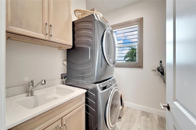 laundry area featuring stacked washing maching and dryer, cabinets, sink, and light hardwood / wood-style floors