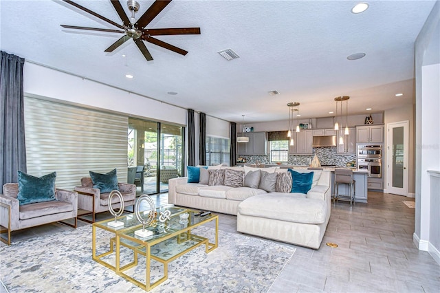 living room featuring a wealth of natural light, ceiling fan, and a textured ceiling