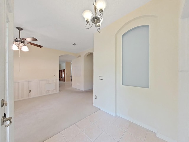 spare room with light carpet, light tile patterned floors, ceiling fan with notable chandelier, and wainscoting