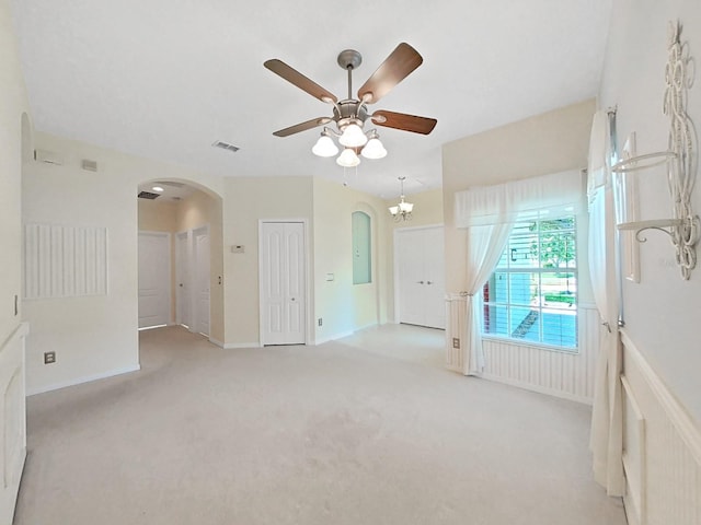 carpeted spare room with visible vents, arched walkways, and a ceiling fan