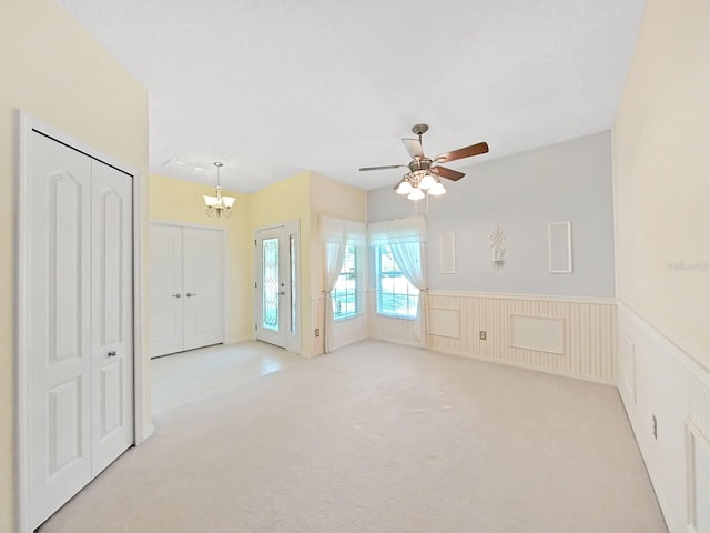 spare room with carpet floors, wainscoting, and ceiling fan with notable chandelier