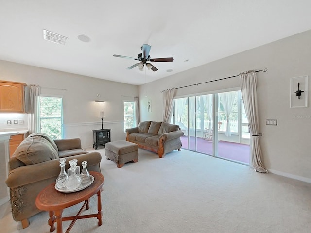 living area with visible vents, baseboards, ceiling fan, carpet floors, and a wood stove