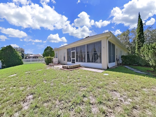 rear view of property with a lawn, fence, a sunroom, and stucco siding