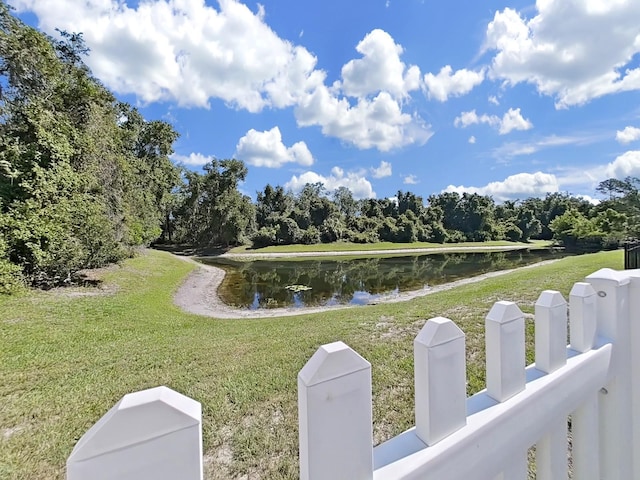 view of community with fence, a lawn, and a water view