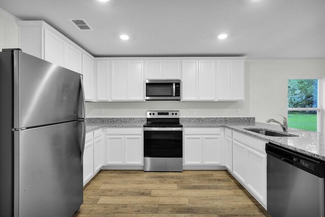 kitchen with stainless steel appliances, white cabinets, and light hardwood / wood-style floors