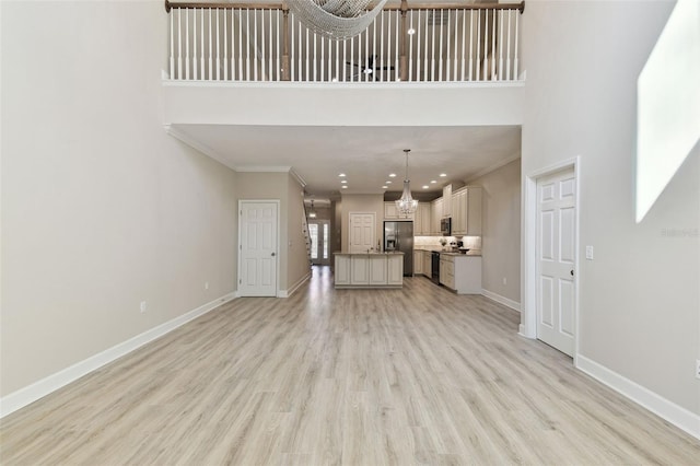 unfurnished living room with light hardwood / wood-style floors, ornamental molding, and a towering ceiling